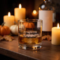 Pour Decision rocks glass 'Hydration* / No Judgment' with whiskey on a big ice cube on a fall home bar with candles and pumpkins, Unhinged Decor