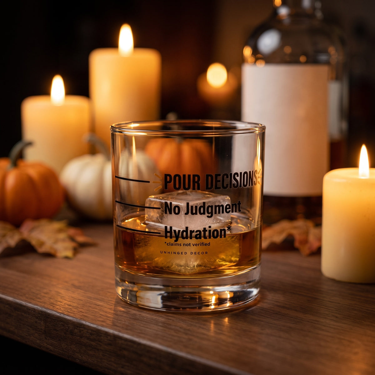 Pour Decision rocks glass 'Hydration* / No Judgment' with whiskey on a big ice cube on a fall home bar with candles and pumpkins, Unhinged Decor