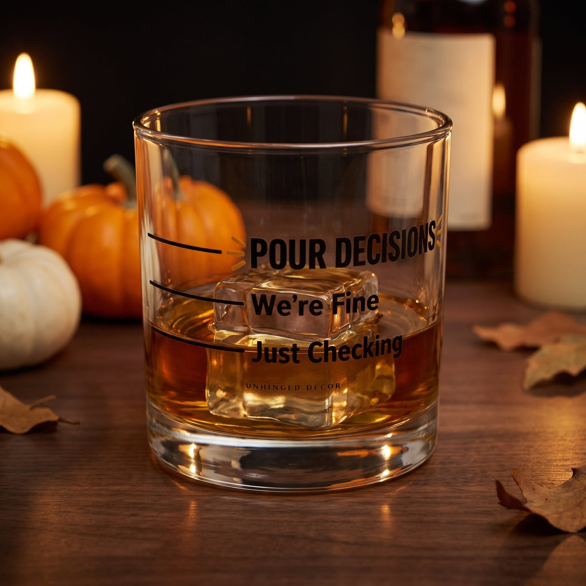 Pour Decision rocks glass 'Just Checking / We’re Fine' with whiskey on a big ice cube on a fall home bar with candles and pumpkins, Unhinged Decor
